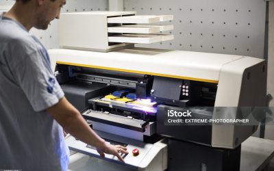 Man is standing inside the printing factory and operating on industrial printer during working hours.